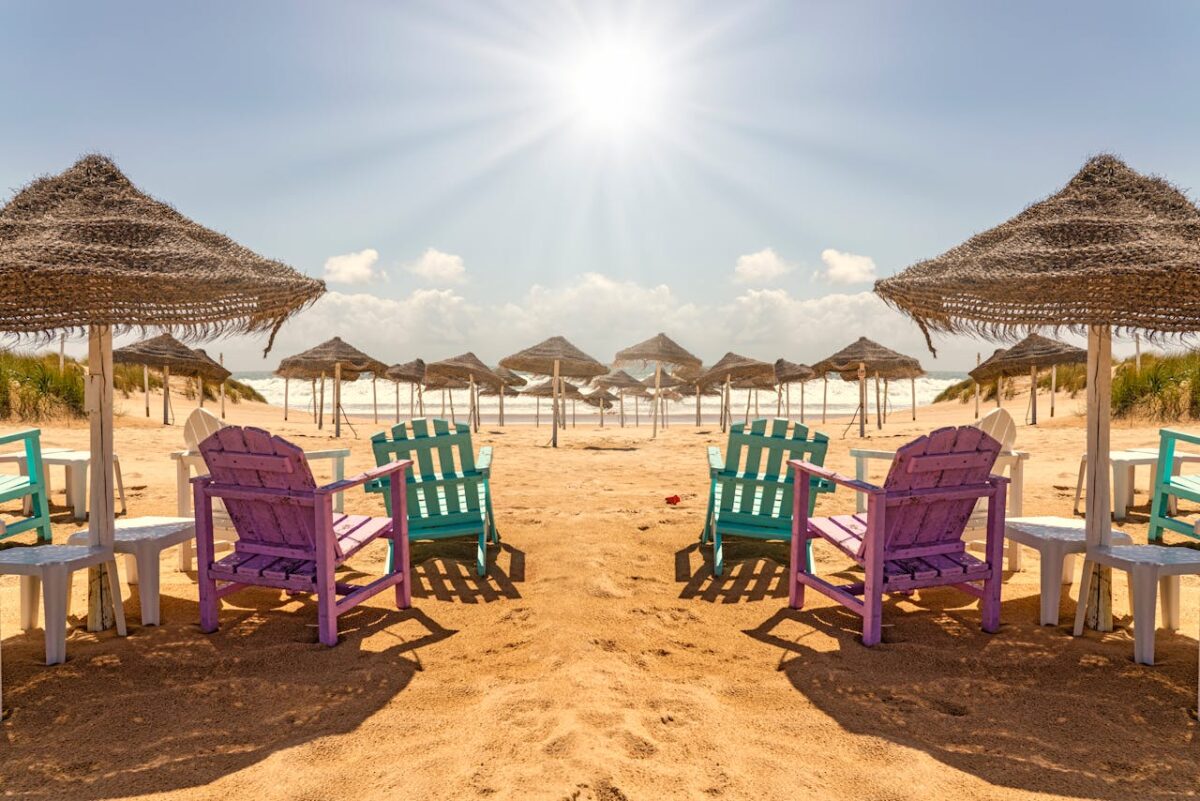 Vibrant colored chairs on a sunny beach with straw umbrellas, epitomizing summer relaxation.